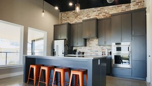 Een moderne keuken met grijze kastjes, een bakstenen muur en een groot kookeiland met barstoelen.