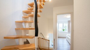 Un escalier moderne avec des marches en bois et une rampe noire, menant à une pièce comprenant un lit et une fenêtre.