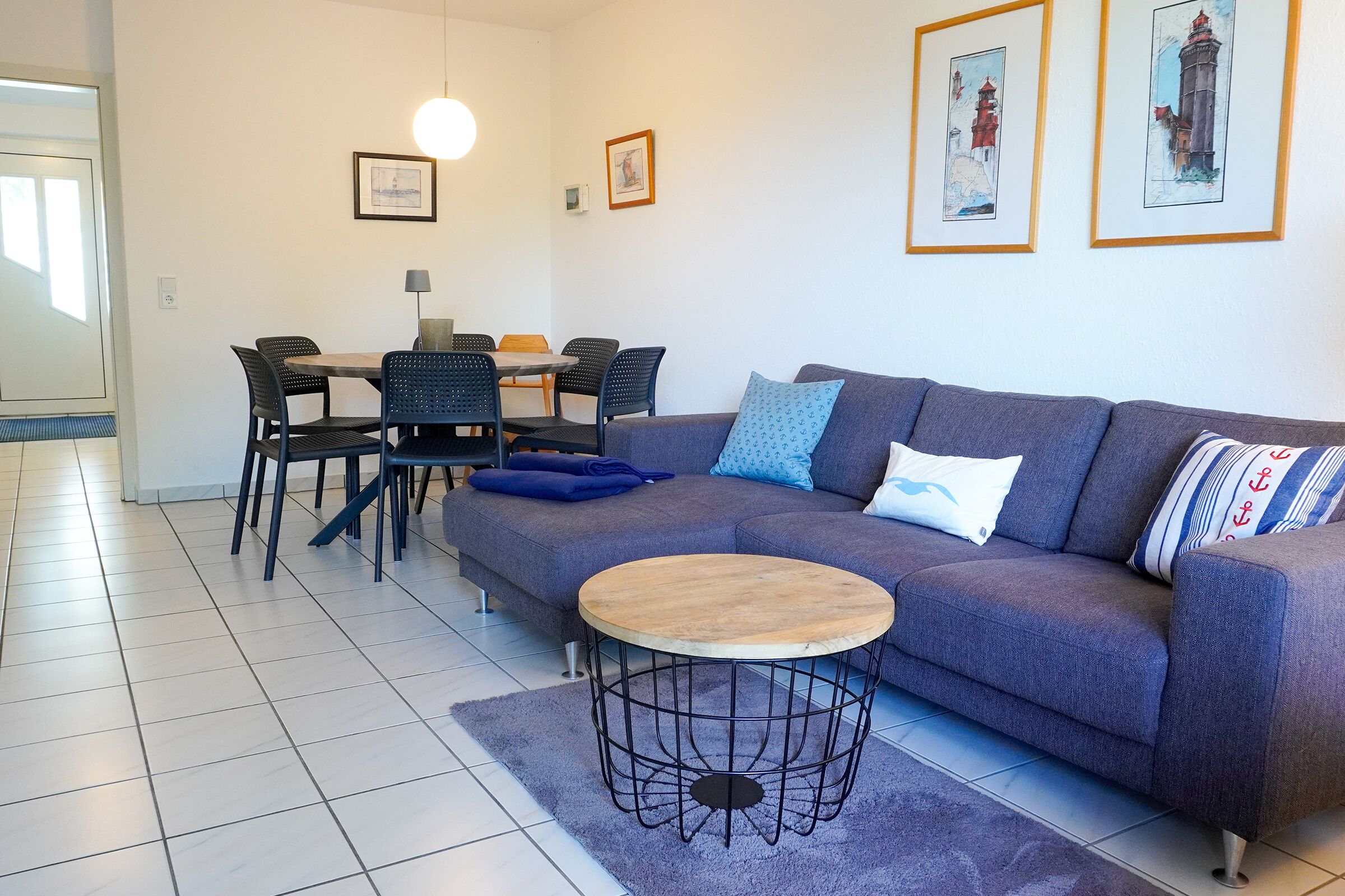Ett modernt vardagsrum med en soffa, ett runt soffbord, ett matbord med stolar och inramade konstverk på väggarna.