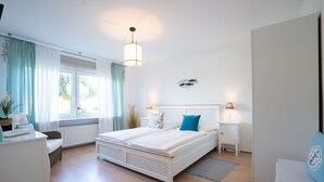 Quarto com cama de casal, mesa de cabeceira com abajur, janela com cortinas e decoração de peixe na parede.