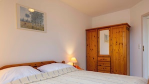 A bedroom with a bed, a wooden wardrobe, a nightstand with a lamp, and a painting on the wall. - Vacation apartment "Musick-Jischa" for up to 2 persons (non-smokers) (Niendorf/Ostsee)