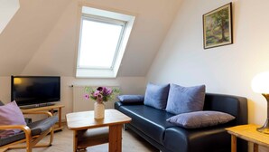 A modern living room with a black leather sofa, a wooden coffee table, a TV on a stand, and a window with a view of the sky. - Vacation apartment "Musick-Jischa" for up to 2 persons (non-smokers) (Niendorf/Ostsee)