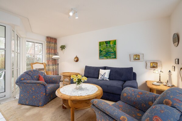 A living room with a sofa, armchairs, a round wooden coffee table, and a painting on the wall.
