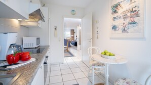 Et moderne køkken med en mikrobølgeovn, en skærebræt med røde peberfrugter, samt et spiseområde med et bord og stole.