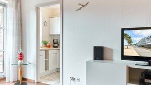 Een moderne woonkamer met een flatscreen televisie, een glazen salontafel en een zichtbare keuken door een open doorgang.
