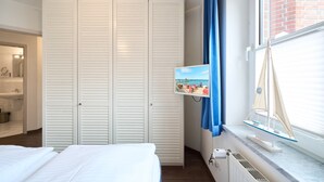 Een slaapkamer met een bed, een kledingkast, een raam met uitzicht op een brug en een klein model zeilboot.