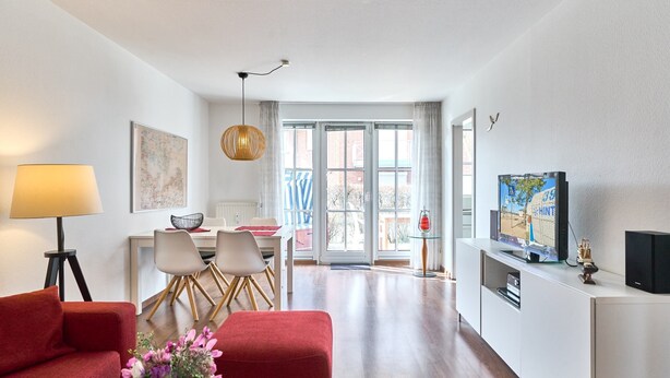 Een moderne woonkamer met een rode bank, een eethoek met stoelen, een televisie en een groot raam met uitzicht.
