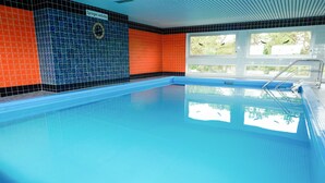 Una piscina interior con pared de azulejos, una ventana y una escalera.