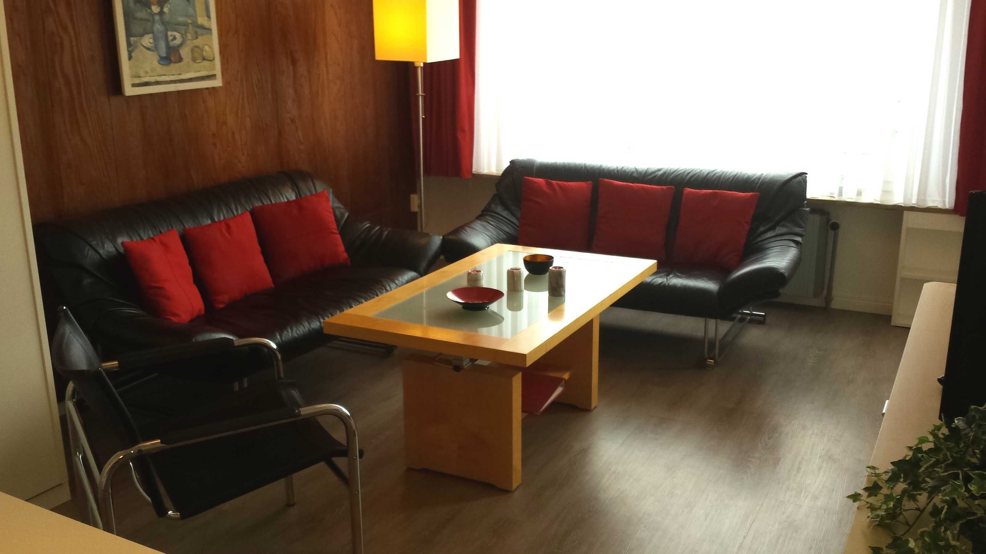 Un espacio habitable compacto con un sofá y sillón de cuero negro, una pequeña mesa de centro de madera y una silla.