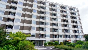 Un edificio residencial de varios pisos con fachada uniforme, balcones y un pequeño acceso con vegetación.