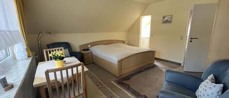 A bedroom with a bed, a desk, a chair, a sofa, and a window with curtains.
