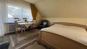 Un dormitorio con una cama grande, un escritorio con una silla, un radiador y una ventana con cortinas.