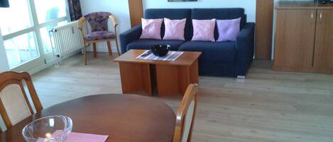 A living room with a wooden dining table, a glass bowl, and a sofa with pink cushions.