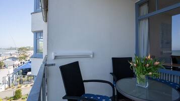Een balkon met twee stoelen en een tafel, een helder uitzicht over de stad, en een vaas met bloemen.