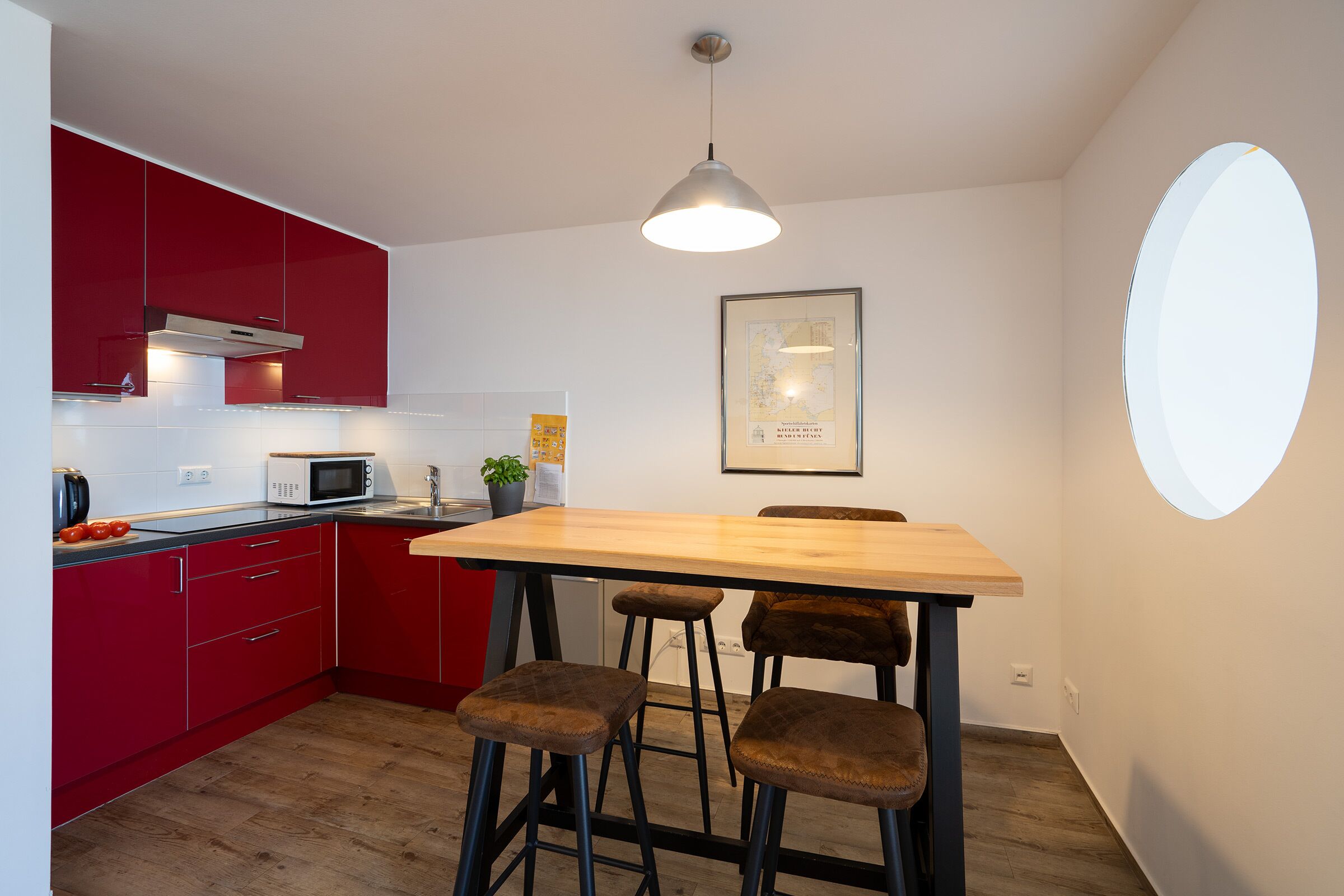 Een kleine keuken met rode kastjes, een houten eettafel en barkrukken.