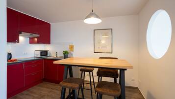Een kleine keuken met rode kastjes, een houten eettafel en barkrukken.