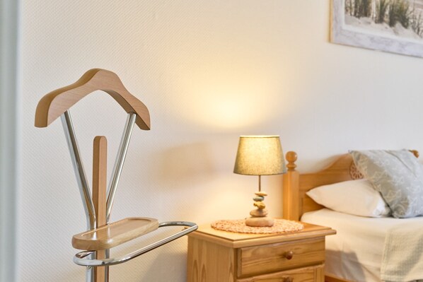Une table de chevet en bois avec une lampe, un lit avec des oreillers et un objet en bois fixé au mur.