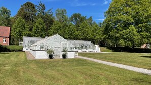 A greenhouse with a glass roof, surrounded by a well-maintained lawn and trees. - Parkhuset  (Hadsund)