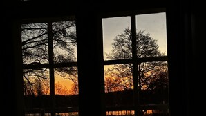 A window with a view of trees and a sunset. - Parkhuset  (Hadsund)