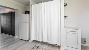 Un baño moderno con cortina de ducha, un armario blanco y un refrigerador.