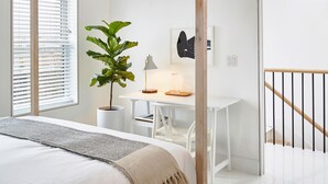 Ein Schlafzimmer mit einem Himmelbett, einem Schreibtisch, einem Stuhl, einer Zimmerpflanze und einer Treppe.