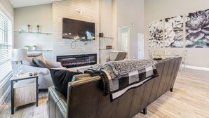 A modern living room with a sofa, a fireplace, a TV mounted on the wall, and a large floral artwork. - Modern Villa Retreat in Saddlebrook Resort (Zephyrhills)