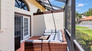 A covered patio with a wicker sofa and a table, a large window, and a view of a residential street. - Modern Villa Retreat in Saddlebrook Resort (Zephyrhills)