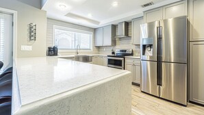 A modern kitchen with a large island, stainless steel appliances, and a window with blinds. - Modern Villa Retreat in Saddlebrook Resort (Zephyrhills)