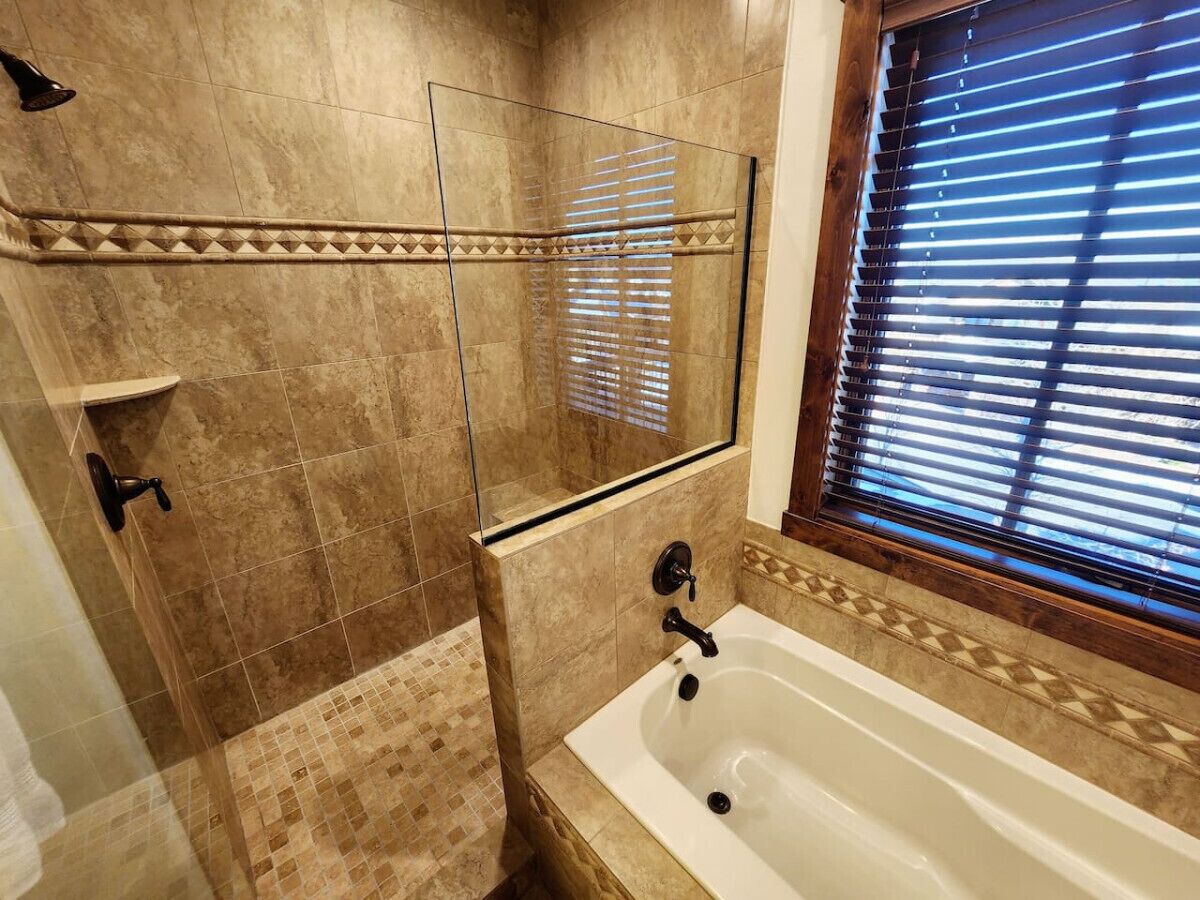 Une salle de bain avec une douche à parois de verre, une baignoire et une fenêtre équipée de stores.