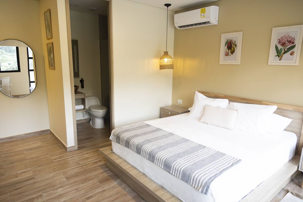 Une chambre à coucher comprenant un lit, une table de chevet, un climatiseur fixé au mur et des reproductions botaniques encadrées.