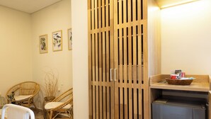 A room with a wooden wardrobe, wicker chairs, a small refrigerator, and framed botanical prints on the wall. - Mythical Hotel (Medellín)