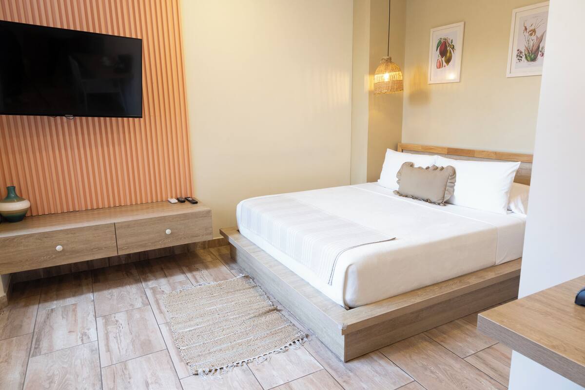 Une chambre moderne avec un téléviseur à écran plat fixé sur un mur recouvert de panneaux en bois, un lit avec une literie blanche, une table de chevet et un tapis tissé.