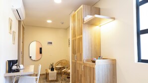 A compact room with a wooden wardrobe, a small table with a chair, a round mirror, and a window. - Mythical Hotel (Medellín)