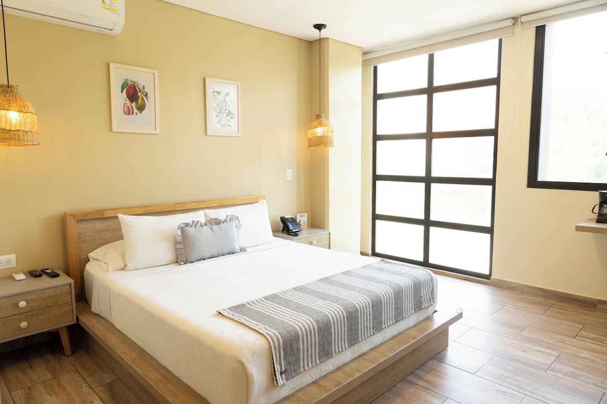 Une chambre d’hôtel avec un grand lit, des tables de chevet, une fenêtre avec des stores et des œuvres d’art accrochées au mur.
