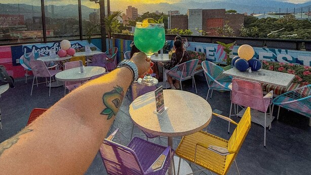 A rooftop bar with outdoor seating, a view of the cityscape, and a sunset in the background. - Mythical Hotel (Medellín)