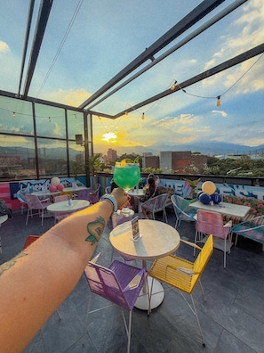 A rooftop bar with outdoor seating, a view of the cityscape, and a sunset in the background. - Mythical Hotel (Medellín)
