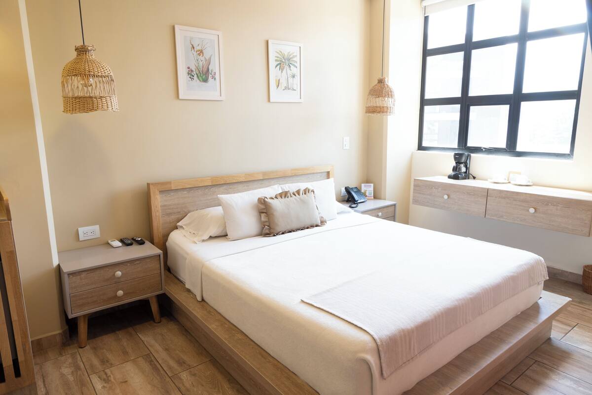 Une chambre à coucher avec un grand lit, des tables de chevet, une commode, une coiffeuse et une fenêtre donnant sur un beau paysage.