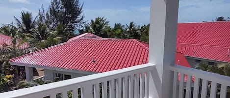Un balcón con barandillas blancas y techo de tejas rojas, con vistas a una zona residencial con tejados similares y palmeras.