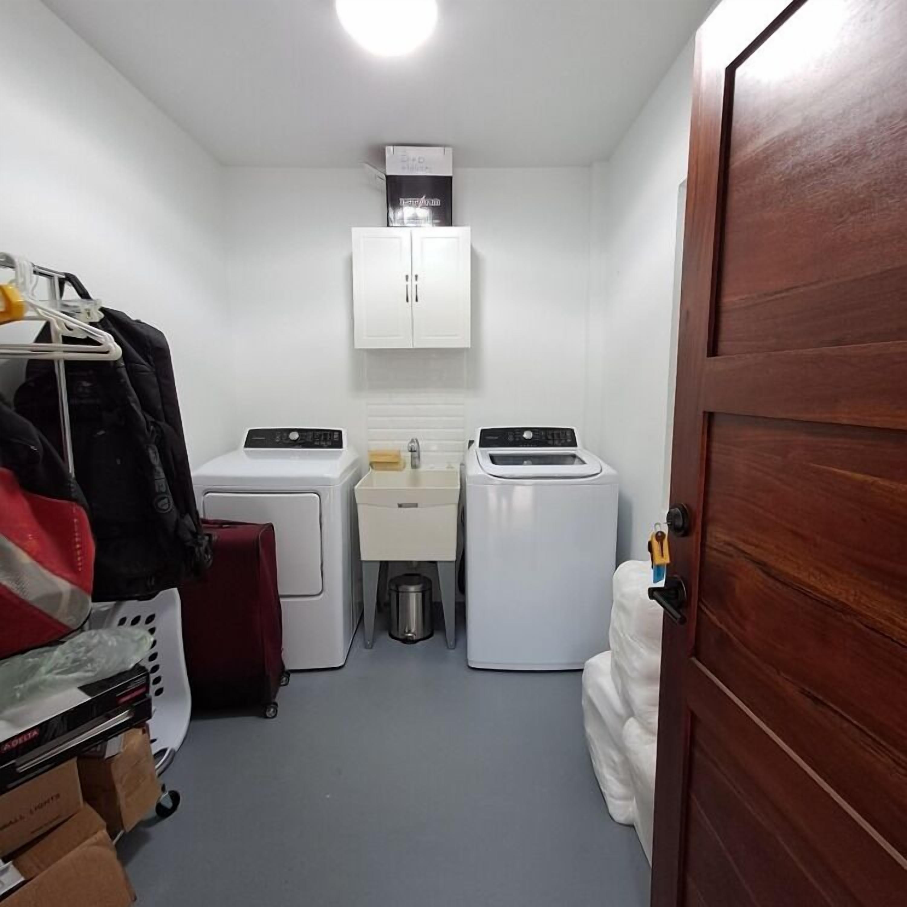 A compact laundry room with two washing machines, a dryer, a small sink, and a cabinet.