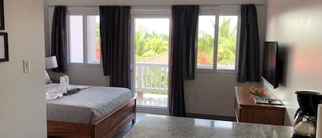 A hotel room with a bed, a desk, a TV, a ceiling fan, and a balcony with curtains.