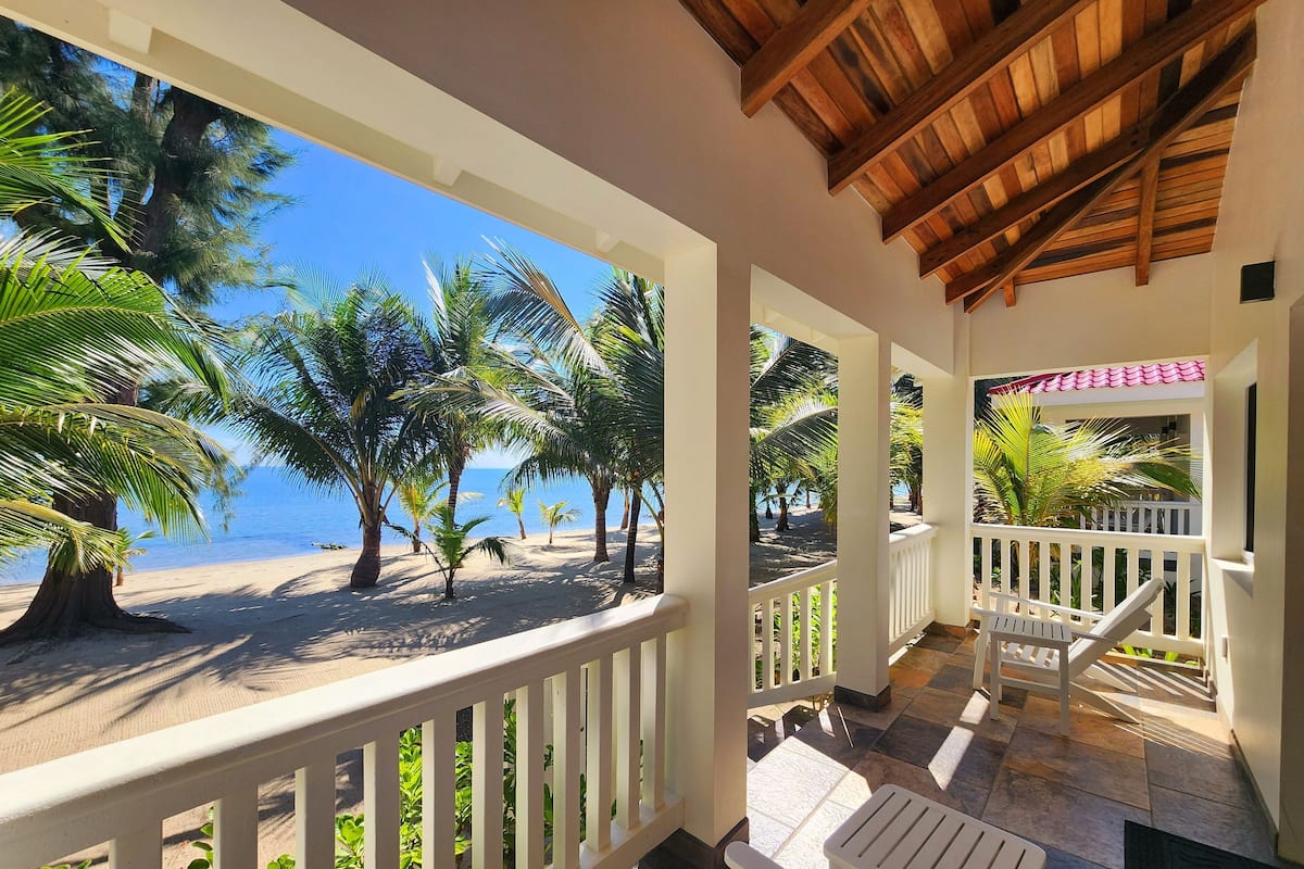 A covered outdoor area with a view of the beach and palm trees.