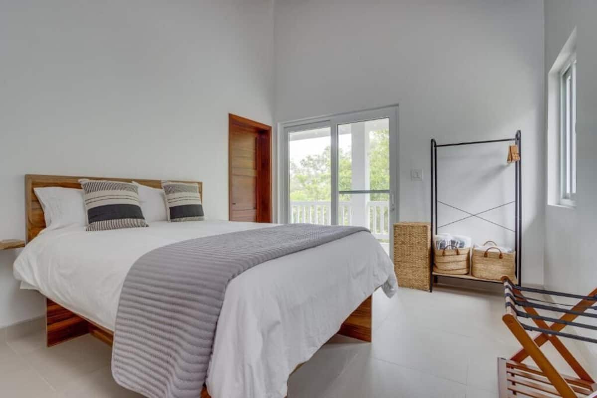 A bedroom with a bed, a wooden headboard, a window, a door, and a rack with baskets.
