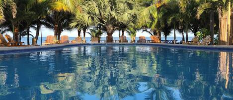 A clear pool with reflections of palm trees and a view of the sea.