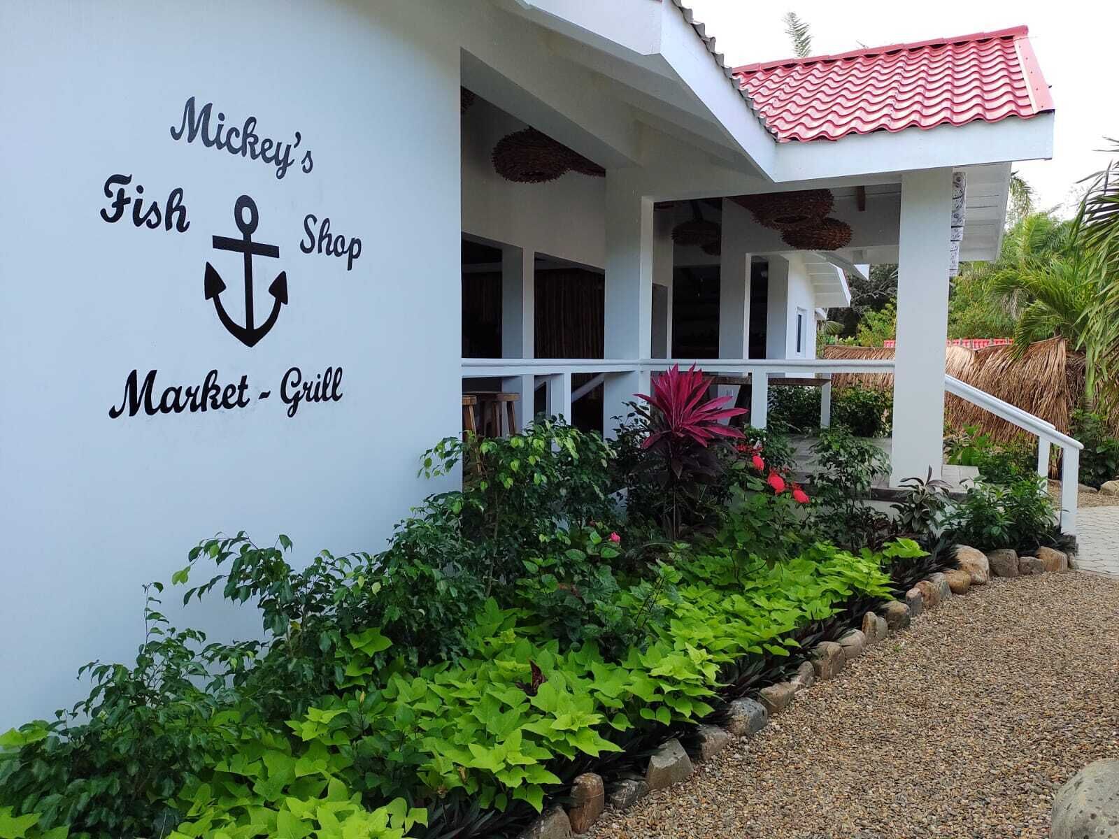 Restaurante e mercado Mickey's Fish Shop Market Grill, com fachada branca, telhado vermelho e escadas que levam à entrada.