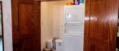 A compact laundry room with a built-in washer and dryer, wooden doors, and a small basket.