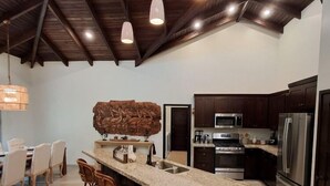 A modern kitchen with dark wooden cabinets, stainless steel appliances, and a central island with bar stools. - Ceiba Beach Resort (Placencia)