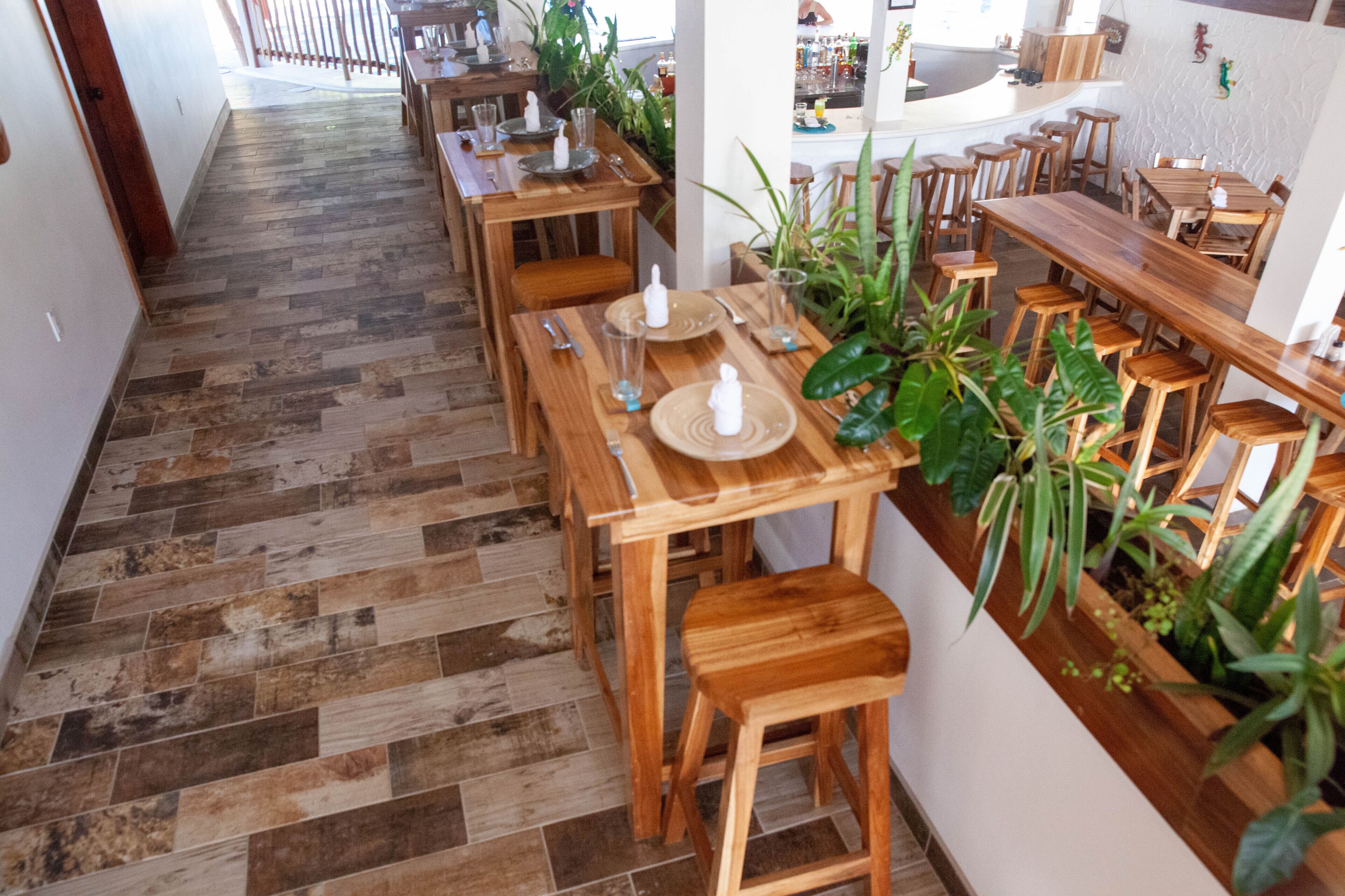 A restaurant with wooden tables and chairs, a herringbone-patterned floor, and potted plants.