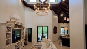 A spacious living room with a large TV, a white sofa, and a chandelier. - Ceiba Beach Resort (Placencia)
