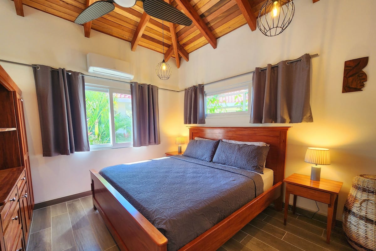 A bedroom with a wooden bed, two bedside tables, a window with curtains, and a ceiling fan.