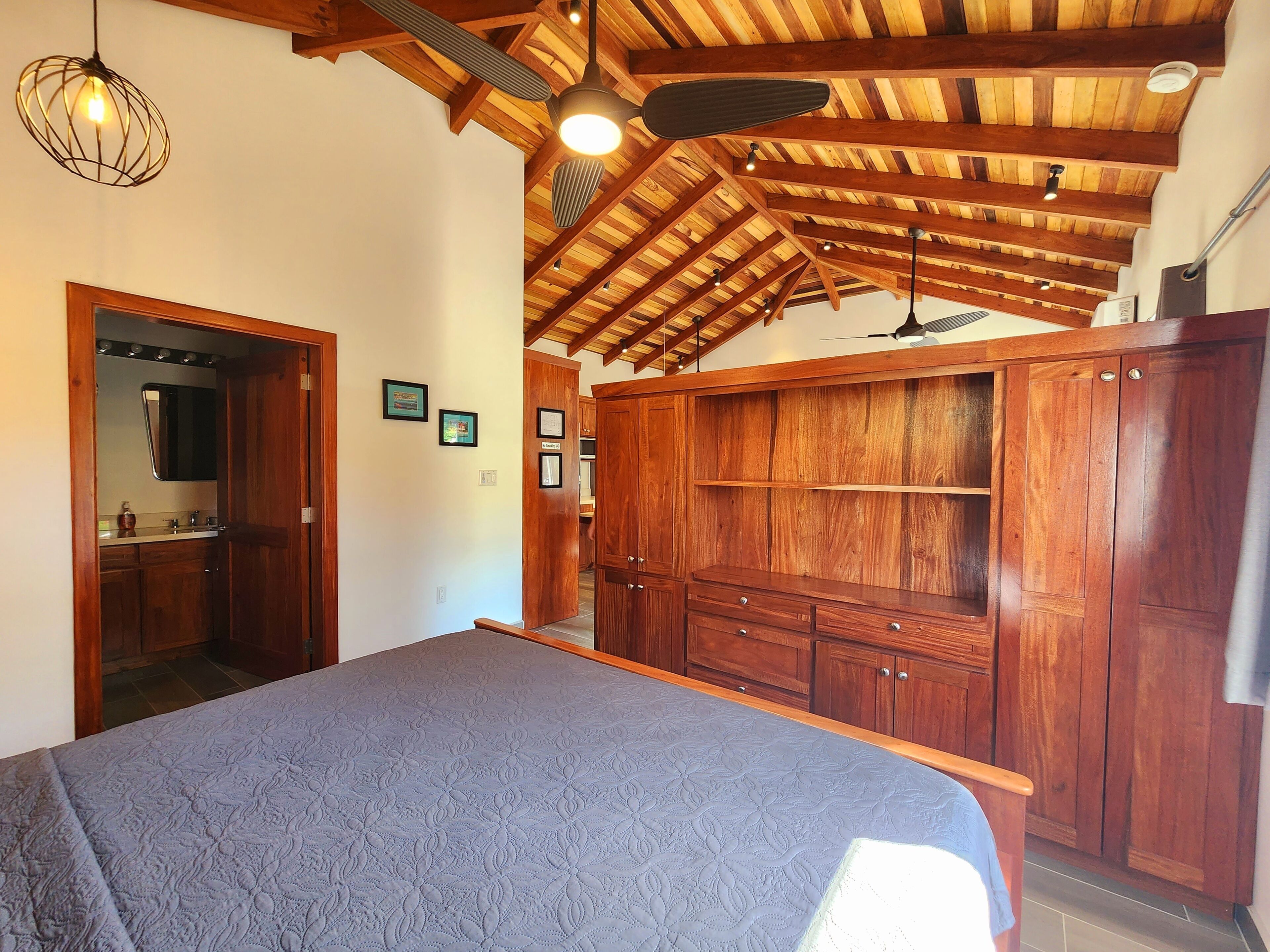 A bedroom with a bed, wooden ceiling beams, and built-in wooden cabinets.